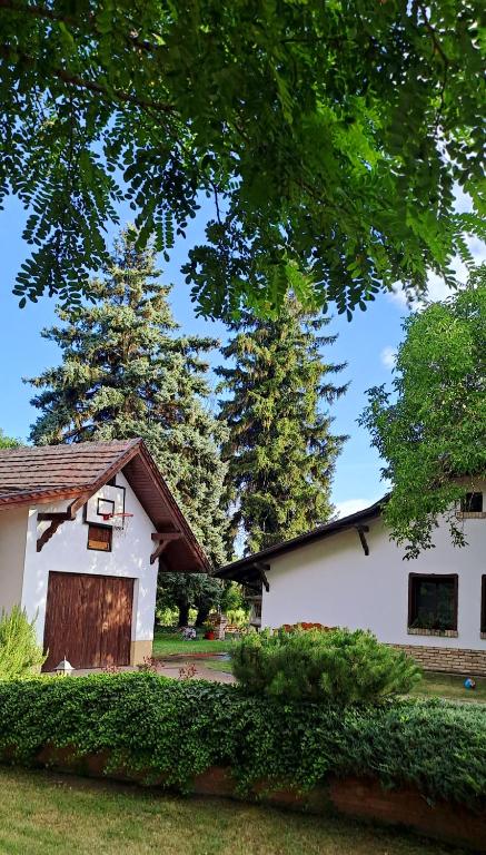 a white house with a garage and two trees at Lassu Tanya Vendégház in Nagykőrös