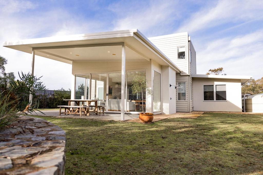 a white house with a large covered patio at Baileys Beach House in Binalong Bay