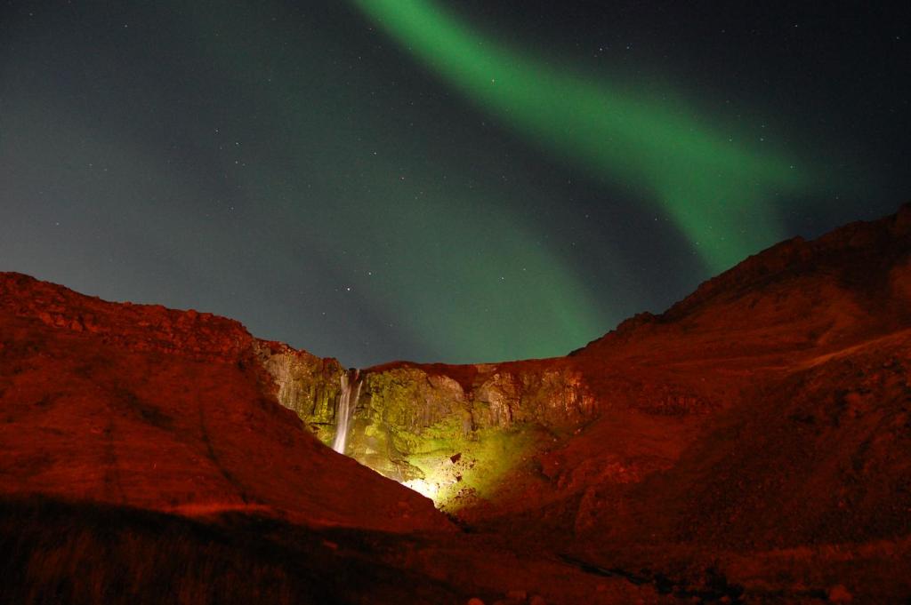 uma aurora brilha sobre uma montanha com uma cascata em North Star Hotel Olafsvik em Ólafsvík