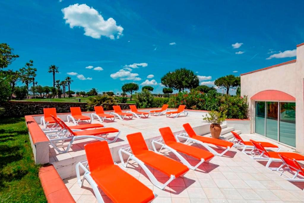 a row of orange lounge chairs on a patio at Vacancéole - Résidence Le Palmyra Golf in Cap d'Agde