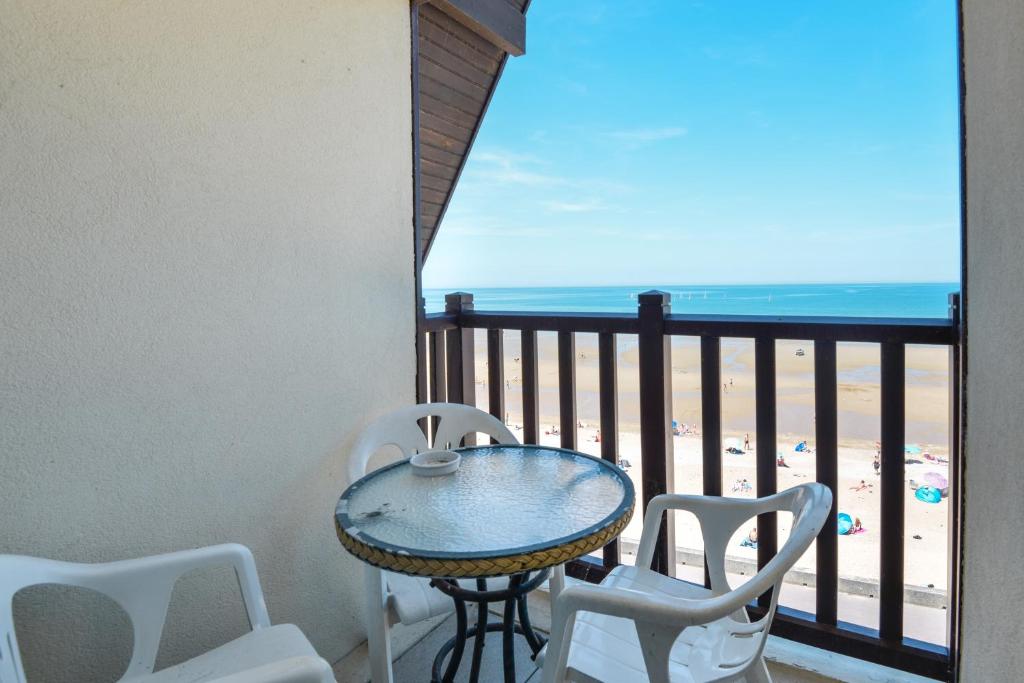 une table et des chaises sur un balcon avec vue sur la plage dans l'établissement Sur la Promenade Proust - Appt vue mer, à Cabourg
