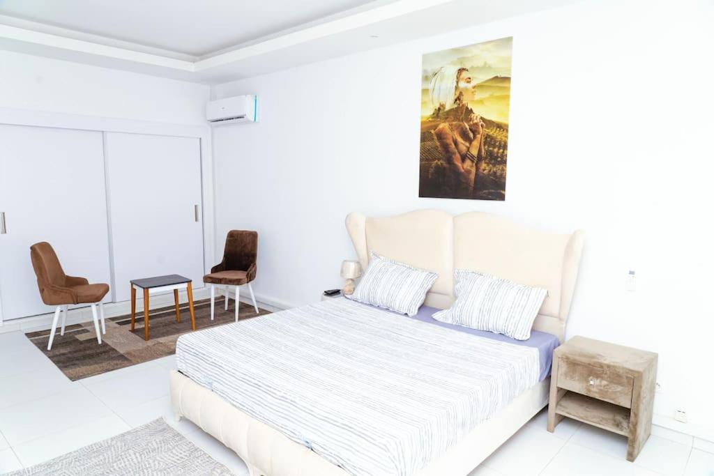 a white bedroom with a large bed and chairs at Séjour Luxe à Mermoz - Confort & Emplacement Idéal in Dakar