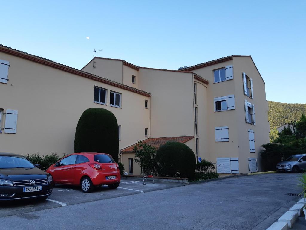 une voiture rouge garée dans un parking à côté d'un bâtiment dans l'établissement Résidence oceane, à Amélie-les-Bains-Palalda