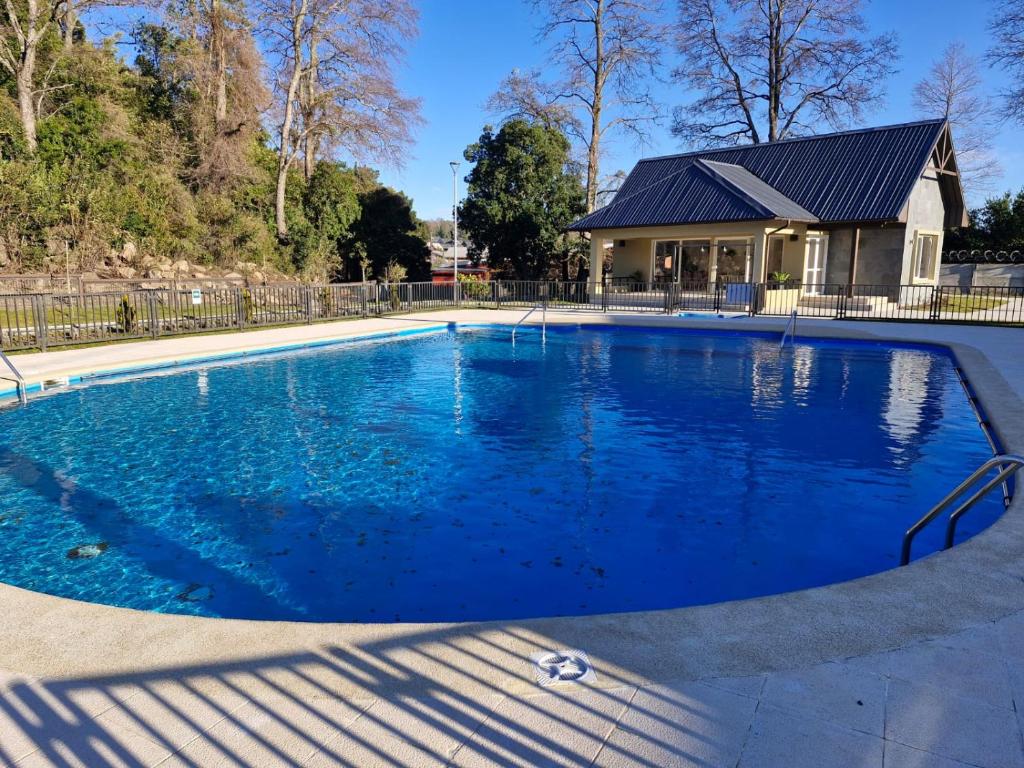 een groot blauw zwembad met een huis op de achtergrond bij Hermosa casa en pucon in Pucón
