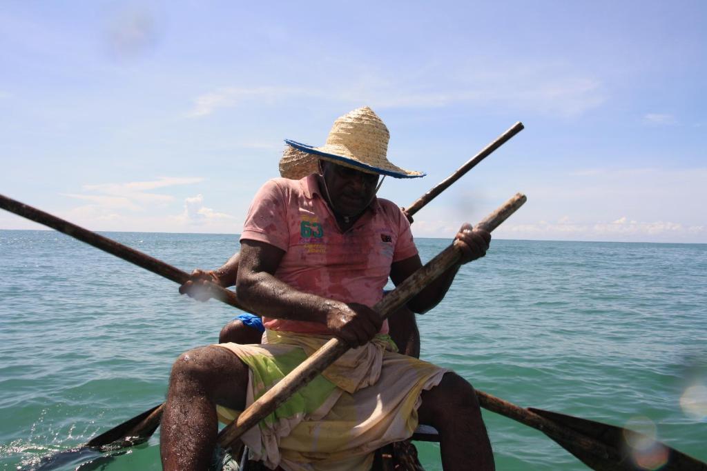 Ein Mann in einem Boot mit zwei Paddeln im Wasser. in der Unterkunft Fishermens Lodge & Restaurant in Ranna