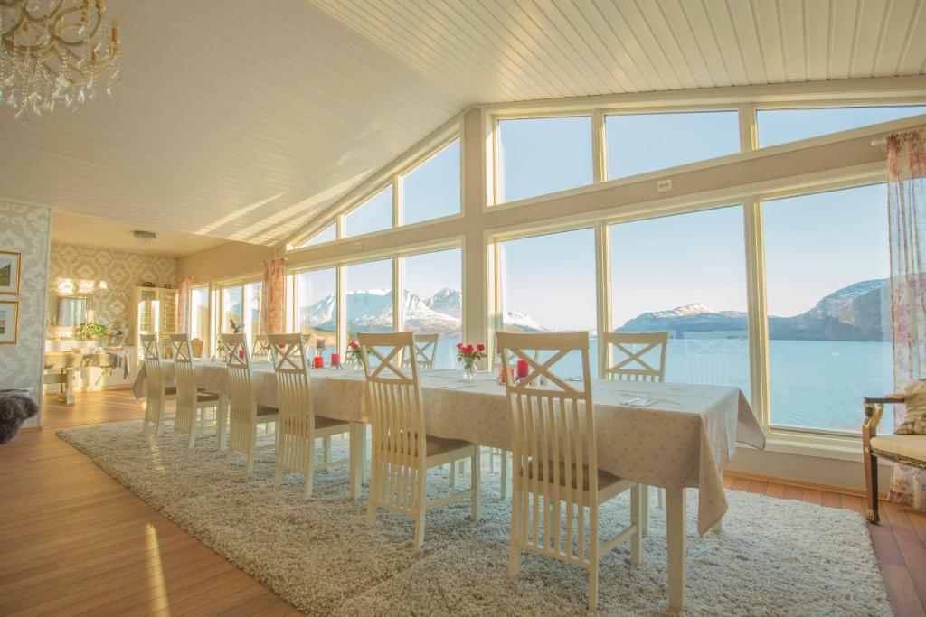 uma sala de jantar com uma mesa longa com cadeiras e janelas em Arctic Panorama Lodge em Uløybukta