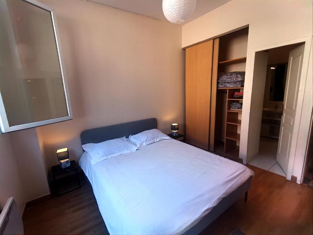 - une chambre avec un lit avec des draps blancs et 2 lampes dans l'établissement Simplicité et confort, à Saint-Fons