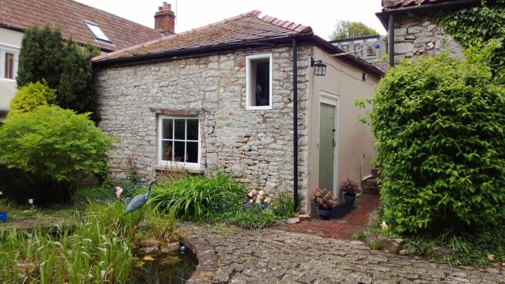 a stone house with a pond in front of it at Longbridge Cottage in Shepton Mallet
