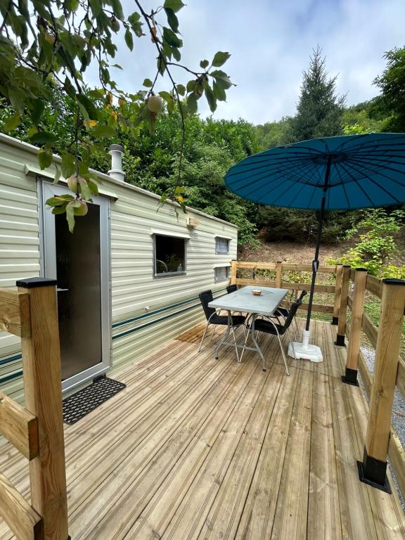 une terrasse en bois avec une table et un parasol dans l'établissement Mobil-home Vintage au bord de la rivière, à Tardets-Sorholus