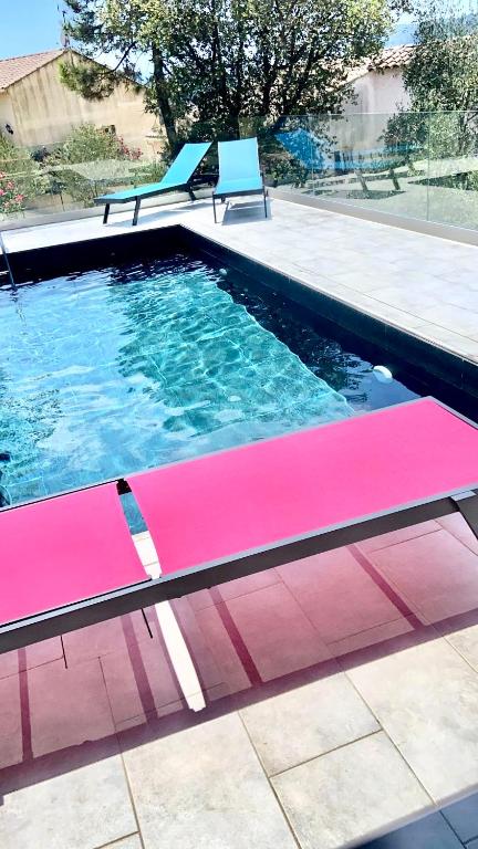 une piscine avec des bancs roses et bleus dans l'établissement Villa Floralie, à Vidauban
