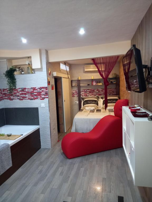 a room with a bed with a red couch and a television at Loft "Coqueto" Rojo in Ubrique
