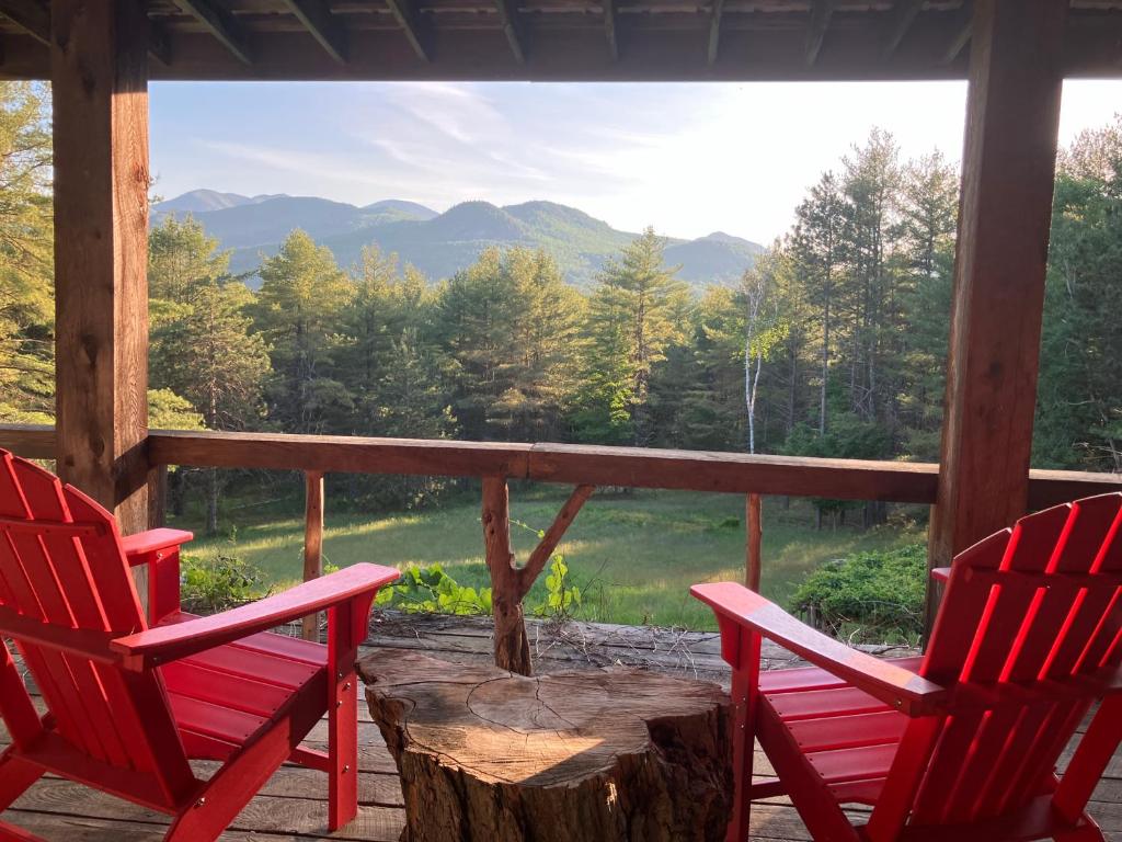 two red chairs sitting on a porch with a tree stump at Adirondack Mountain View Retreat in Elizabethtown