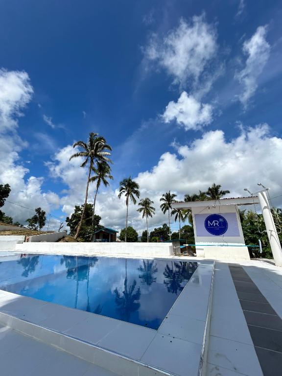 a swimming pool in front of a building with palm trees at Malabuyoc Resort Cebu in Cerdeña