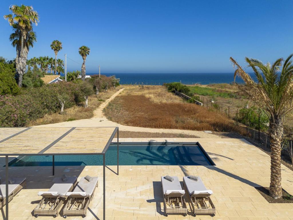 ein Swimmingpool mit Stühlen und das Meer im Hintergrund in der Unterkunft Villa Calamare - IsulaTravel in Avola