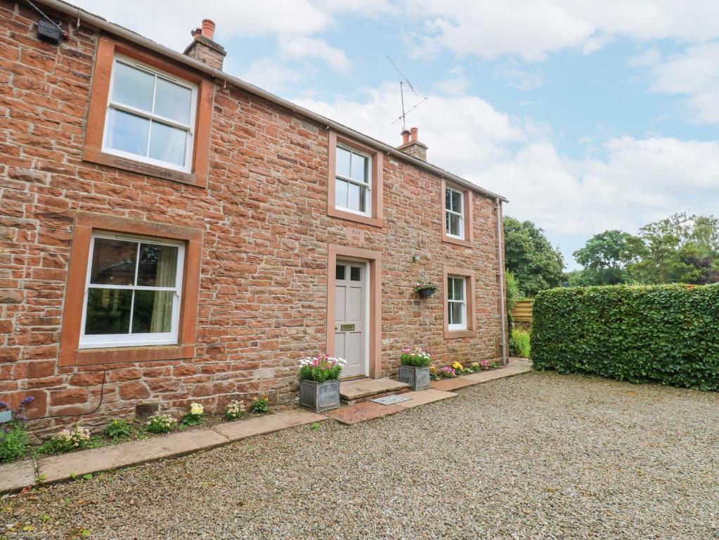 ein Backsteinhaus mit zwei Fenstern und einer Auffahrt in der Unterkunft Garden Cottage in Penrith