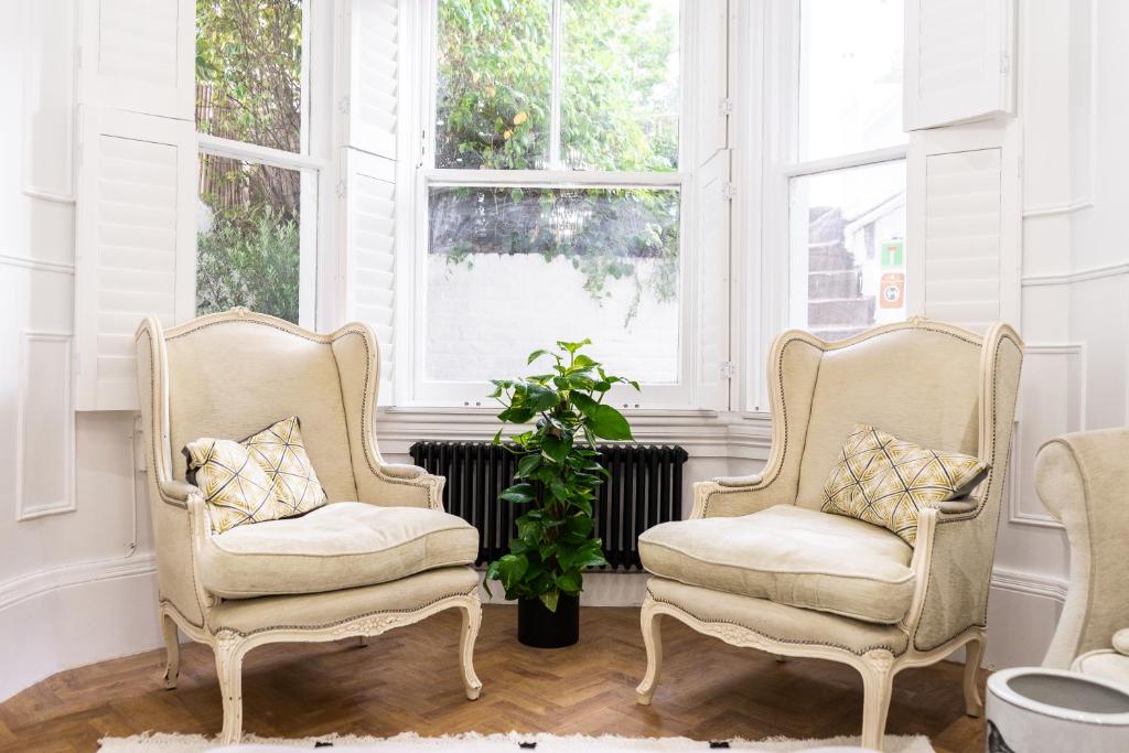two chairs and a plant in a room with windows at Kensington Bay View Dreams in London