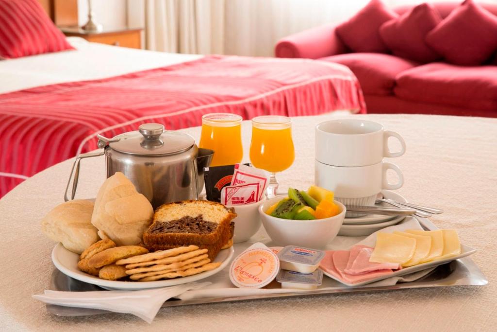 una bandeja de alimentos para el desayuno y bebidas en una cama en Hotel Montecarlo Santiago, en Santiago