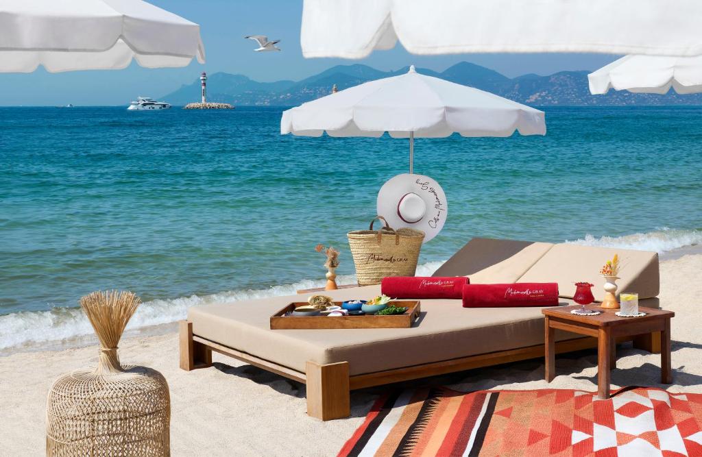 a bed on a beach with an umbrella and a table at Hôtel Barrière Le Gray d'Albion in Cannes