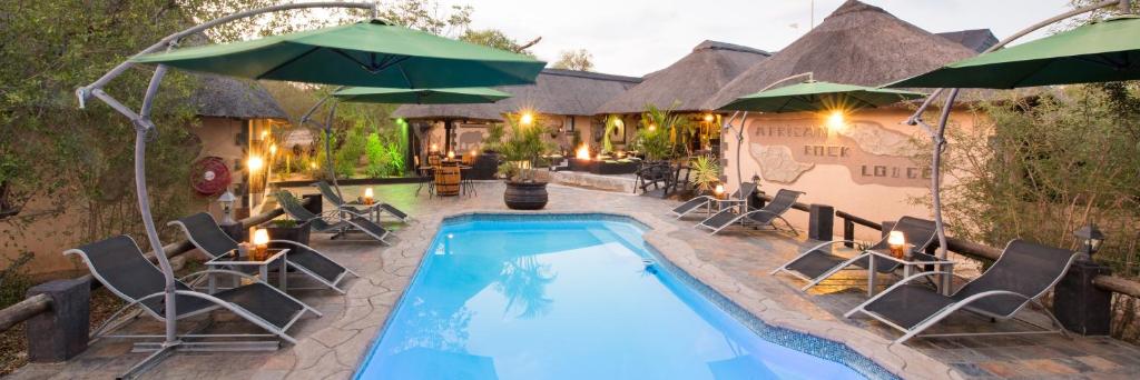 a pool with chairs and umbrellas next to a house at African Rock Lodge in Hoedspruit