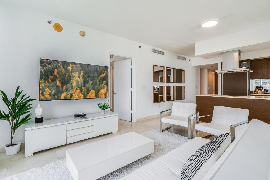 a living room with white furniture and a large screen tv at ICON Brickell Miami- 2 bedroom Condo with City and water views! in Miami