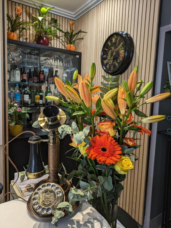 eine Vase mit Blumen auf einem Tisch mit einer Uhr in der Unterkunft Virgina in Paris