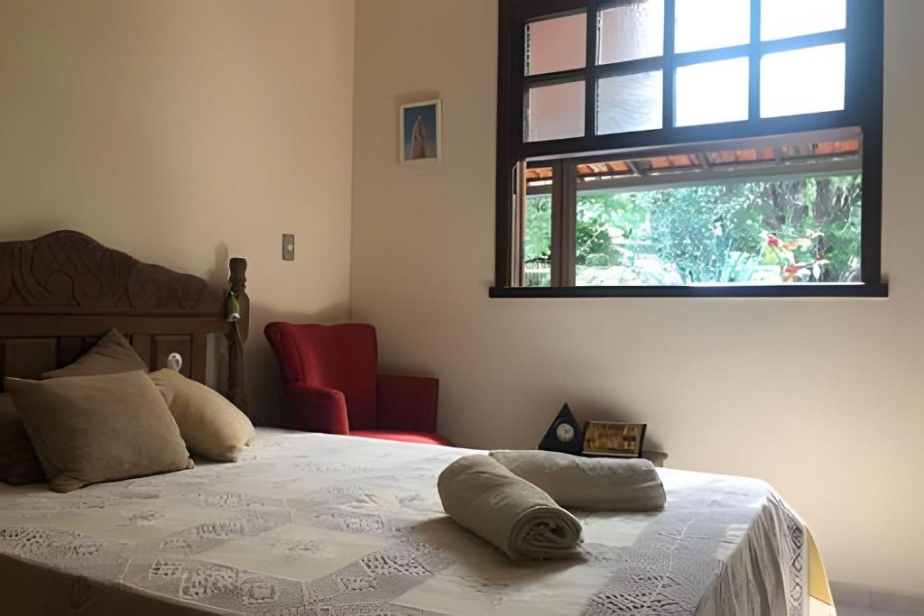 a bedroom with a bed with a window and a red chair at Sitio com Piscina AQUECIDa e 5 quartos c/ suíte! in Jaboticatubas