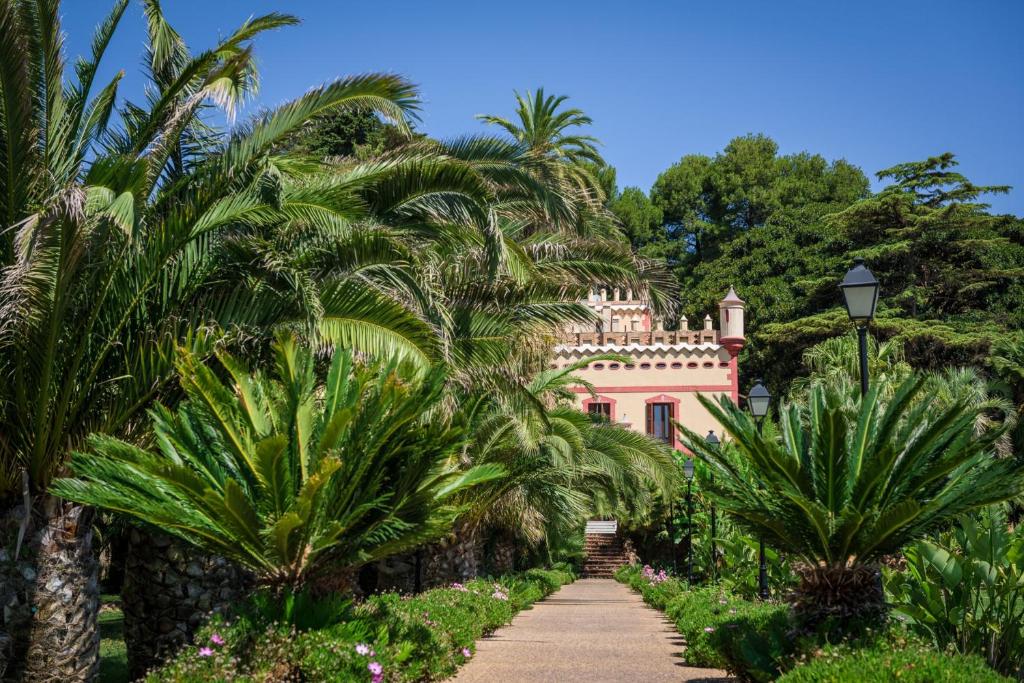 a pink house surrounded by palm trees and a pathway at Hotel Villa Retiro in Xerta