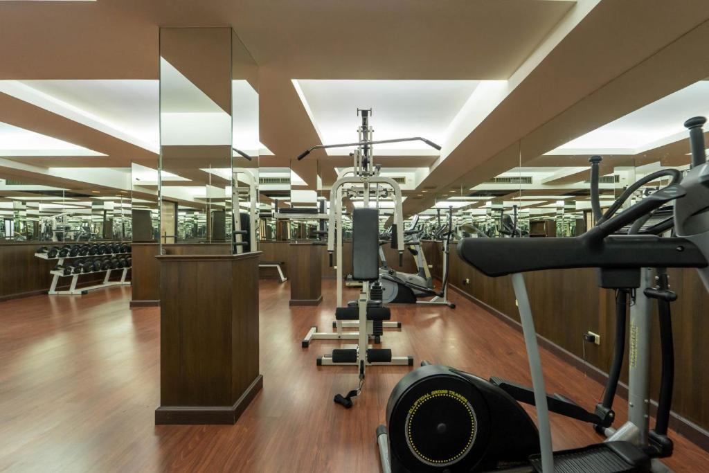 A mirrored fitness room contains cardio machines, weights, and a central multi-station machine.