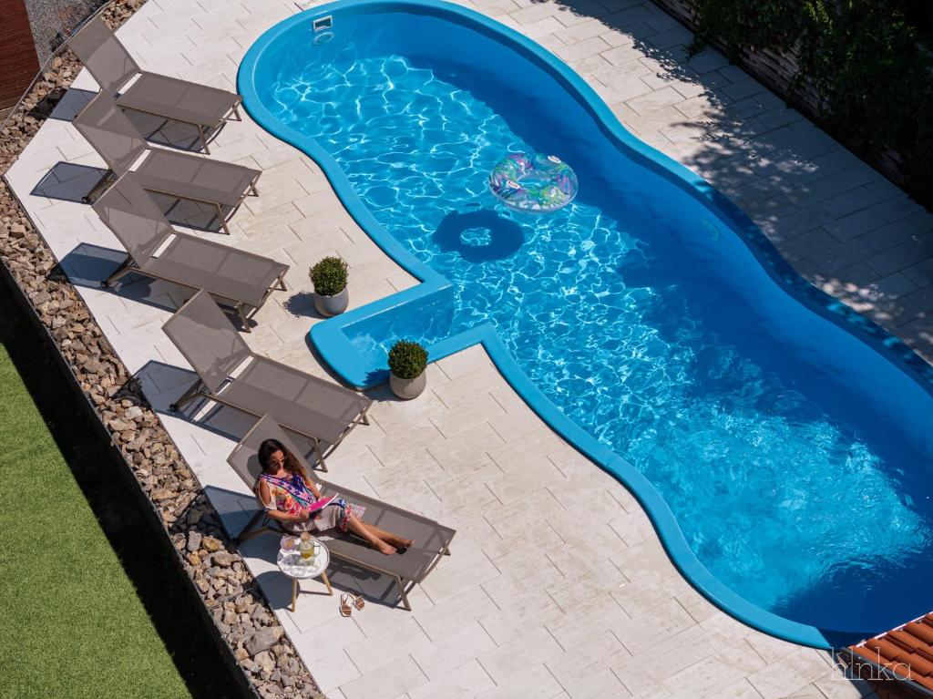 a woman sitting in a chair next to a swimming pool at Délceg Réce Minihotel in Balatonkenese