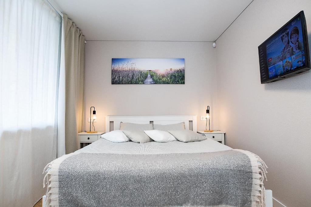 a white bedroom with a white bed with two lamps at Jaukus butas Šiaulių centre #2 in Šiauliai