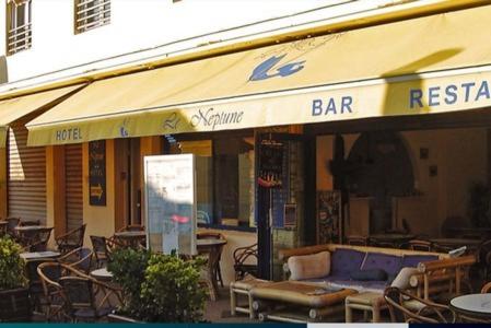 um restaurante com um banco e mesas e cadeiras em Hôtel Le Neptune em Soulac-sur-Mer