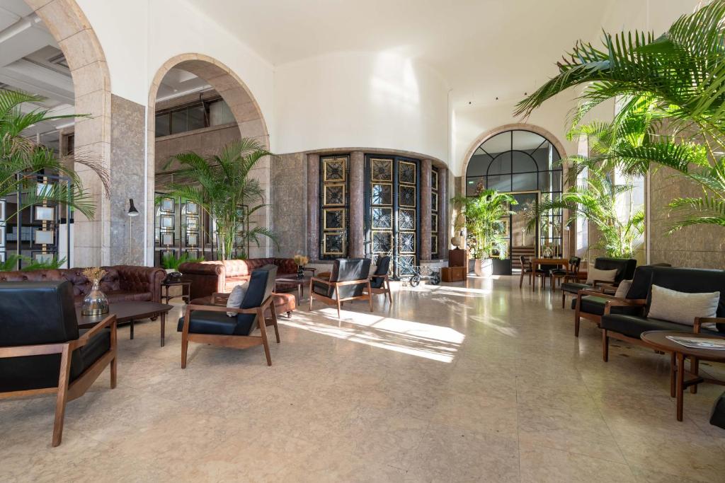 A grand, sunlit lobby with stone arches, palms and generous lounge seating.