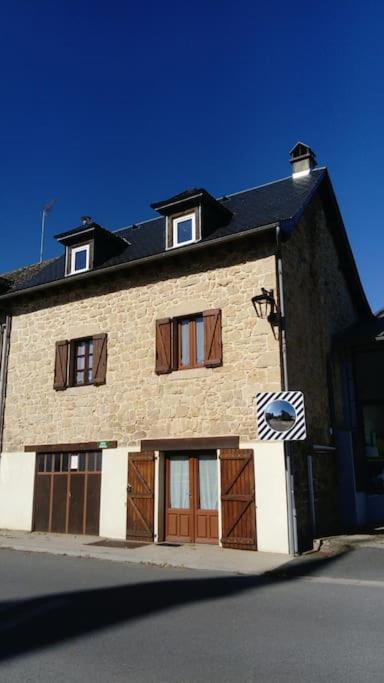 un grand bâtiment en briques avec des portes et un toit noir dans l'établissement Maison au cœur d'un petit village, à Goutrens