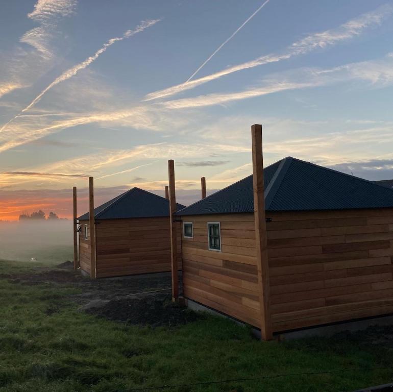 Hooiberghut op boerderij في لايدسخيندام: كوخين خشبيين في حقل مع شروق الشمس في الخلفية