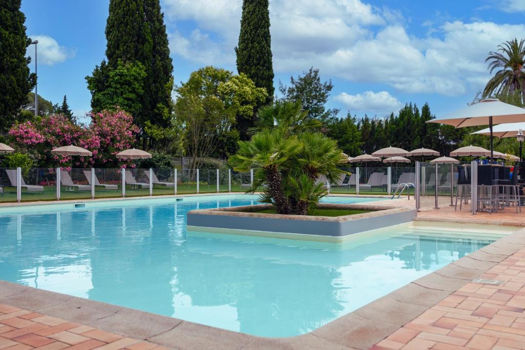 a large swimming pool with trees and umbrellas at Golf Hôtel de Valescure & Spa NUXE in Saint-Raphaël