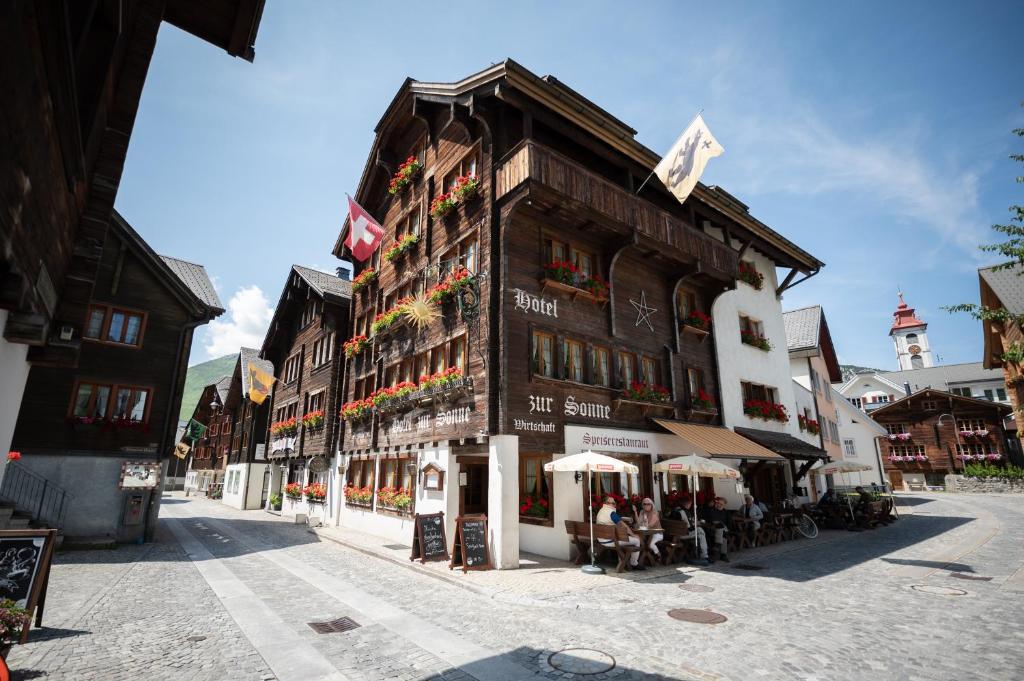 a building on a street with people sitting outside at Sonne Andermatt Swiss Quality Hotel in Andermatt