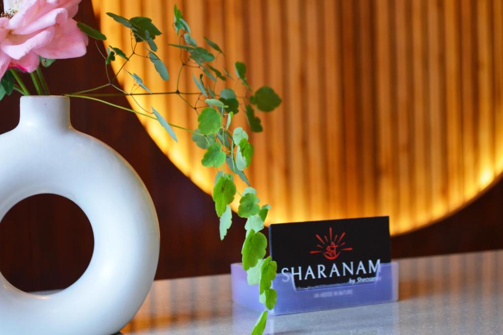 Un jarrón blanco con una tarjeta y flores sobre una mesa. en Sharanam by Sheosante, en Manali