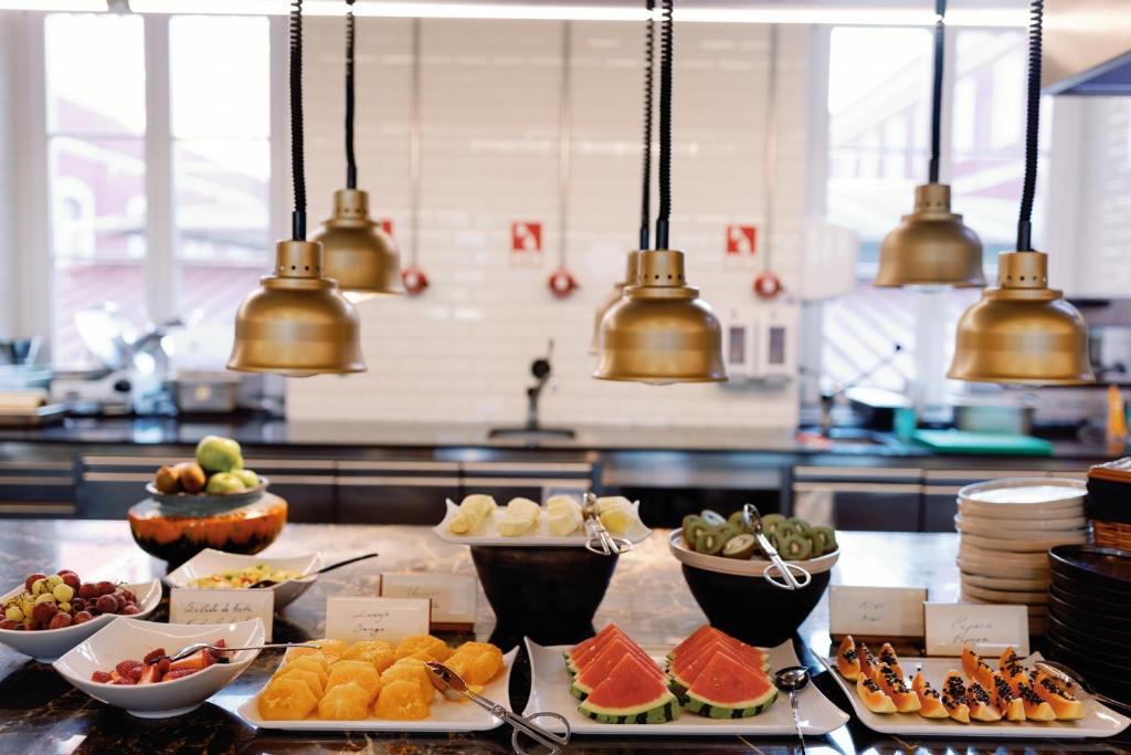 A brightly lit breakfast buffet with fruit, pastries, serving bowls and stacks of plates.