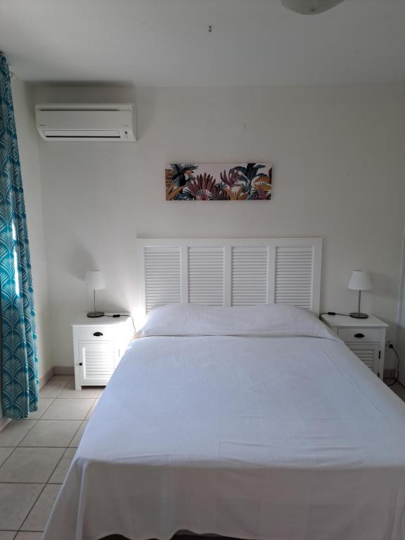 a white bedroom with a white bed and two tables at Résidence les salines in Sainte-Anne