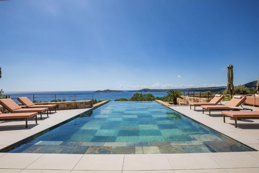 une piscine avec des chaises et l'océan en arrière-plan dans l'établissement Villa Lucia Arinella, à Pinarellu