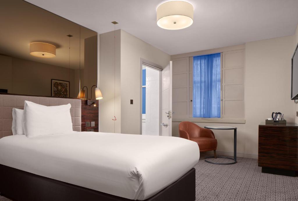 a hotel room with a large bed and a chair at Strand Palace in London