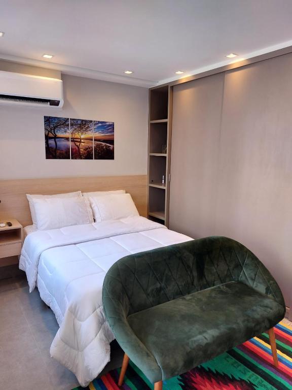 a bedroom with a large bed and a green chair at Studio Giovanni Gronchi - Ao Lado do Metrô in São Paulo
