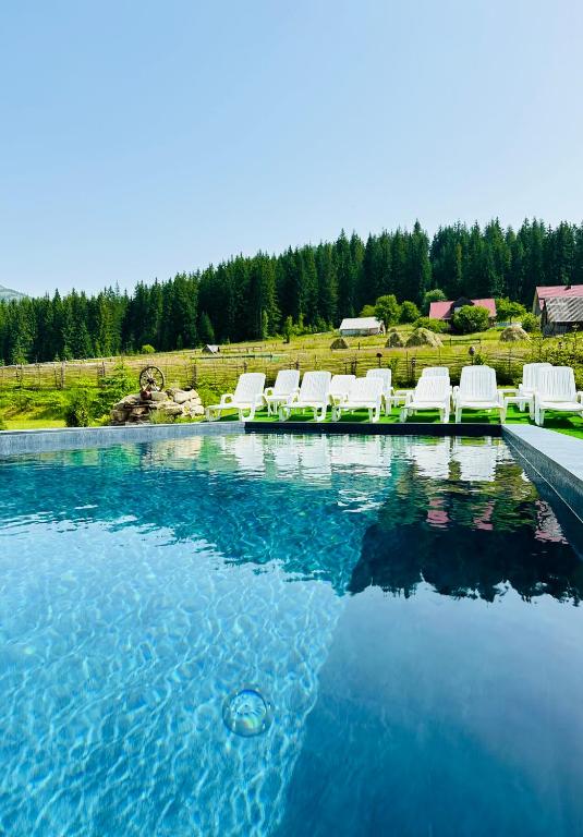 a swimming pool with white chairs and the water at Guest House Lileya in Bukovel