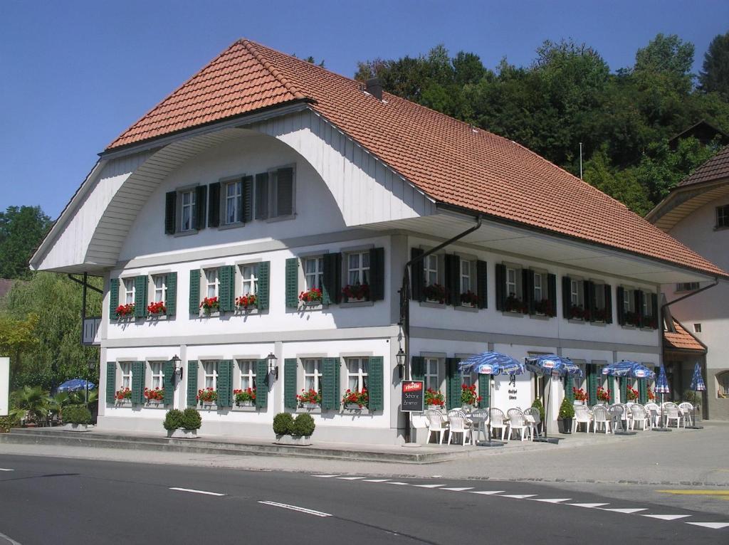 ein weißes Gebäude mit Tischen und Stühlen auf einer Straße in der Unterkunft Gasthof Löwen in Melchnau