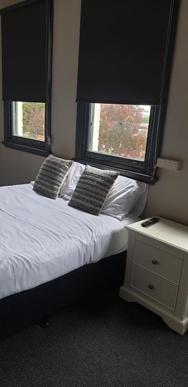 a bedroom with a bed with two pillows and two windows at The Court House Hotel Narromine in Narromine