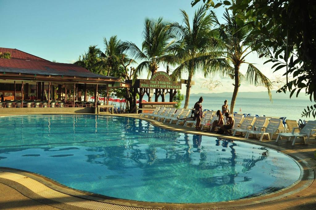 a swimming pool with people sitting in chairs next to the ocean at Coral Bungalows in Haad Rin