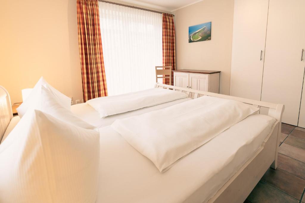 two white beds in a room with a window at Haus Seeschwalbe - Wohnung 15 in Spiekeroog