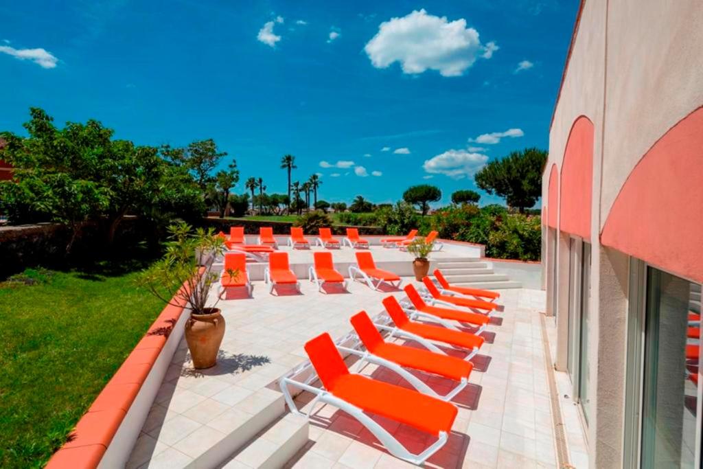 - une rangée de chaises longues orange sur la terrasse dans l'établissement Vacancéole - Résidence Le Palmyra Golf, au Cap d'Agde