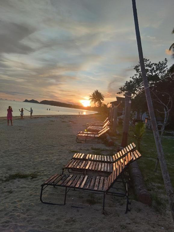a row of benches on a beach at sunset at Ban Tai Bay Bungalows in Ban Tai