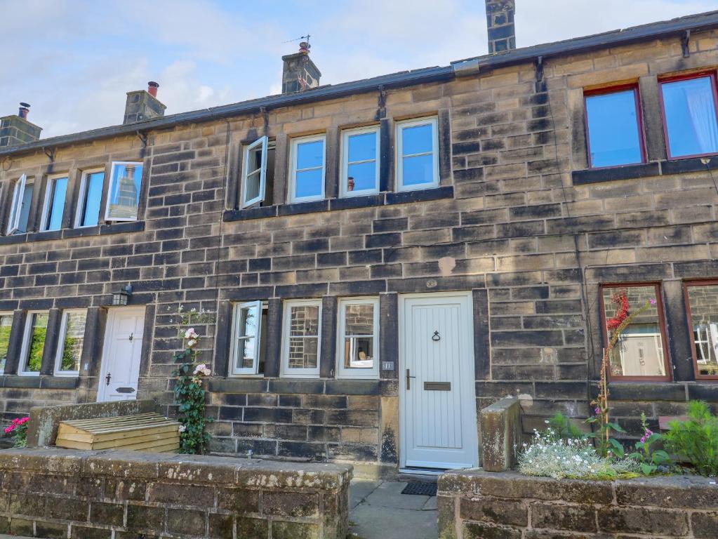 a brick house with a white door and windows at Cobbles Cottage in Heptonstall